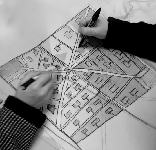 a photograph taken from above of two hands from two people drawing together on a plan of streets